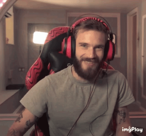A Man With A Beard Is Wearing Headphones And Smiling While Sitting In An Office Chair GIF