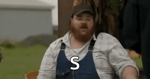 A Man With A Beard Is Wearing Overalls And A Hat And Says The Letter S . GIF
