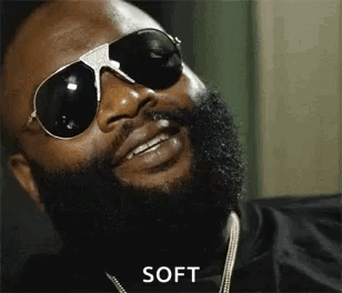A Man With A Beard Is Wearing Sunglasses And A Necklace . GIF