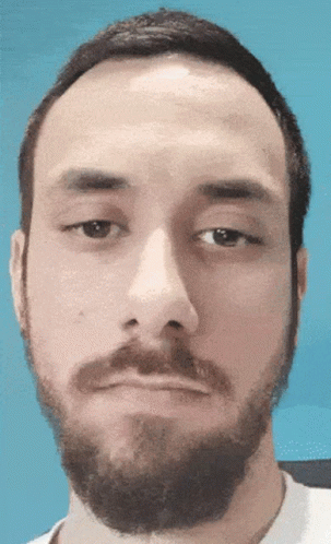 A Man With A Beard Looks At The Camera With A Blue Background GIF