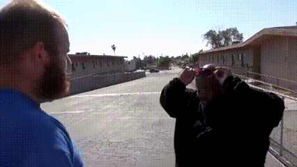 A Man With A Beard Looks Through Binoculars At Another Man GIF