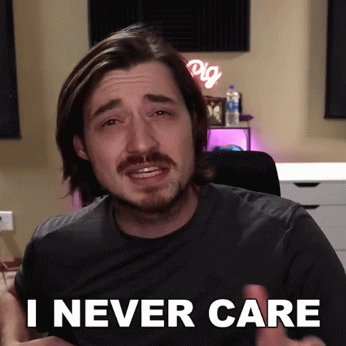A Man With A Beard Says " I Never Care " In Front Of A Desk GIF