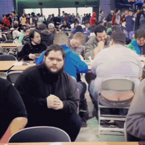 A Man With A Beard Sits In A Crowded Restaurant GIF