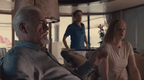 A Man With A Beard Sits On A Couch With A Woman And A Man Standing Behind Him GIF