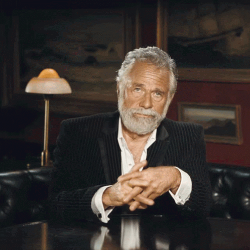 A Man With A Beard Sitting At A Table With His Hands Outstretched GIF