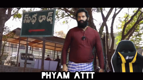 A Man With A Beard Standing In Front Of A Sign That Says Phyam Attt GIF