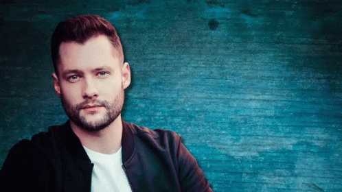 A Man With A Beard Stands In Front Of A Blue Brick Wall GIF
