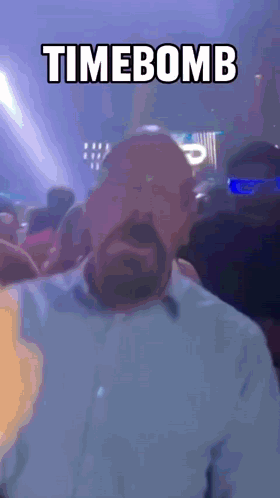 A Man With A Beard Stands In Front Of A Crowd With The Words Timebomb Above Him GIF