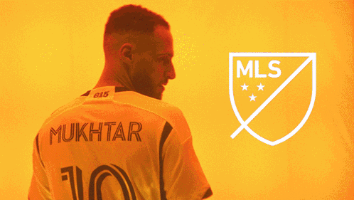 A Man With A Beard Stands In Front Of A Logo For The Mls GIF