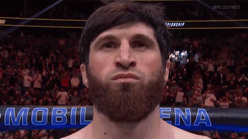 A Man With A Beard Stands In Front Of A Sign That Says Mobil Ena GIF