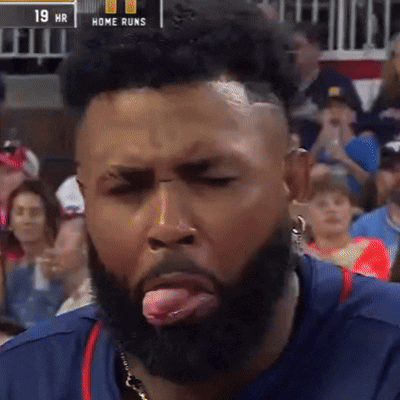A Man With A Beard Sticking His Tongue Out In Front Of A Scoreboard That Says Home Runs GIF