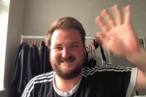 a man with a beard wearing a black and white adidas shirt is waving