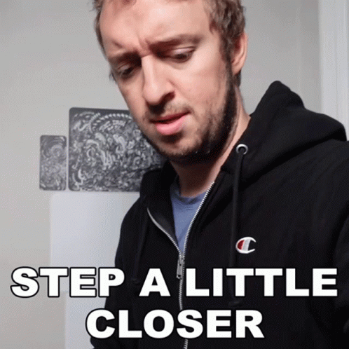 A Man With A Beard Wearing A Black Champion Hoodie Says Step A Little Closer GIF