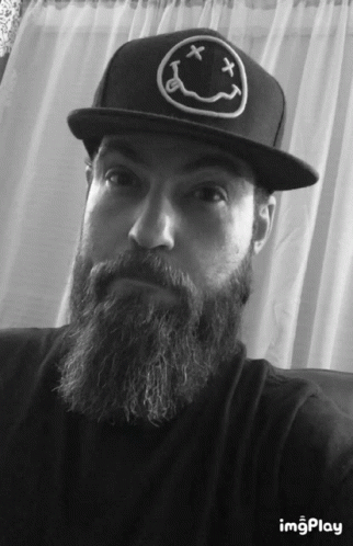 A Man With A Beard Wearing A Black Hat With A Smiley Face On It GIF