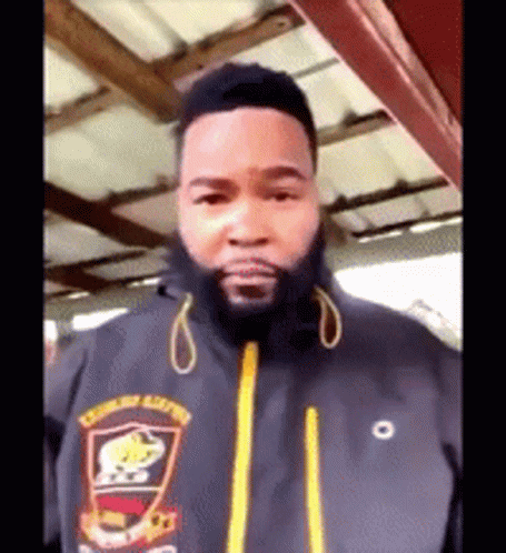 A Man With A Beard Wearing A Black Jacket With A Yellow Zipper GIF
