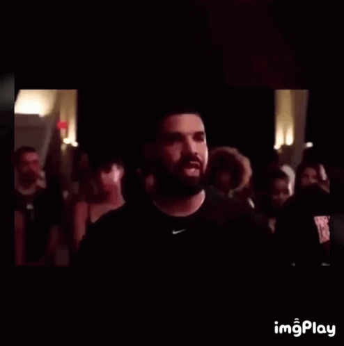 A Man With A Beard Wearing A Black Nike Shirt Stands In Front Of A Crowd Of People GIF