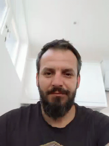 A Man With A Beard Wearing A Black Shirt Is Smiling And Looking At The Camera . GIF