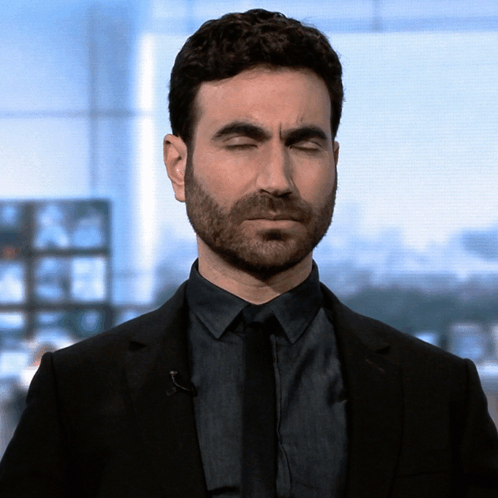 A Man With A Beard Wearing A Black Suit And Tie With His Eyes Closed GIF