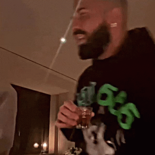 A Man With A Beard Wearing A Black Sweatshirt With Green Letters That Says 99 On It GIF