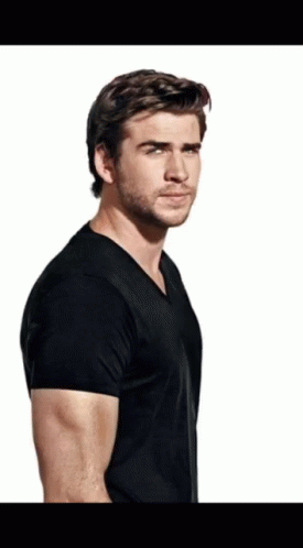 A Man With A Beard Wearing A Black T-Shirt Is Standing In Front Of A White Background GIF