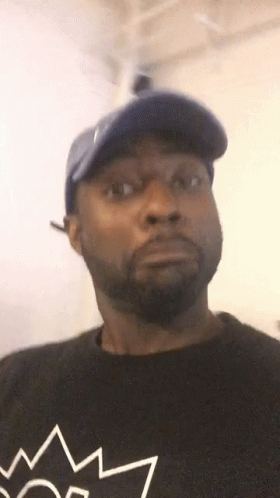 A Man With A Beard Wearing A Blue Hat And A Black Shirt With A Crown On It . GIF