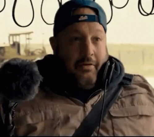 A Man With A Beard Wearing A Blue Hat And A Tan Jacket GIF