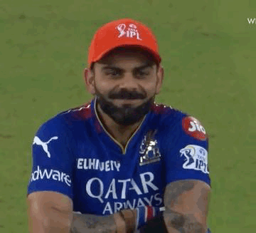 A Man With A Beard Wearing A Blue Shirt And A Red Hat Is Holding A Cricket Ball . GIF