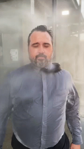 A Man With A Beard Wearing A Blue Shirt And Tie Is Standing In A Foggy Room GIF