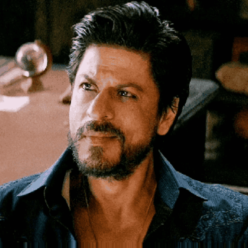 A Man With A Beard Wearing A Blue Shirt Is Looking At The Camera GIF