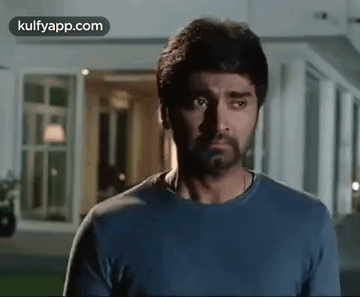A Man With A Beard Wearing A Blue Shirt Is Standing In Front Of A Building . GIF