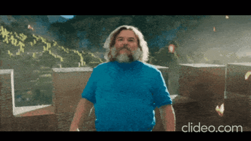 A Man With A Beard Wearing A Blue Shirt Is Standing In Front Of A Pile Of Cardboard Boxes GIF