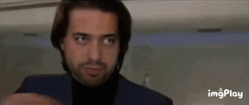A Man With A Beard Wearing A Blue Suit And Black Turtleneck Is Looking Up . GIF