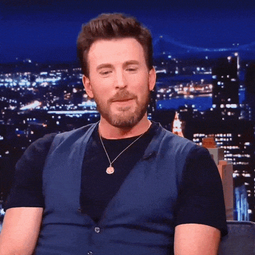 A Man With A Beard Wearing A Blue Vest And Black Shirt GIF