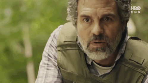 A Man With A Beard Wearing A Bullet Proof Vest Is Looking At The Camera . GIF