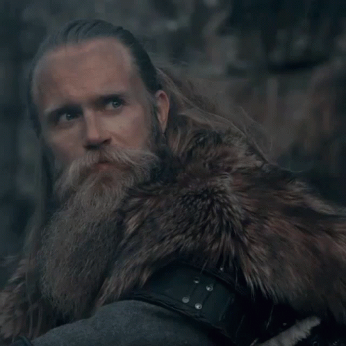 A Man With A Beard Wearing A Fur Coat Looks At The Camera GIF