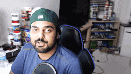 A Man With A Beard Wearing A Green Hat Is Sitting In A Chair GIF