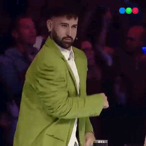 A Man With A Beard Wearing A Green Jacket Stands In Front Of A Crowd GIF
