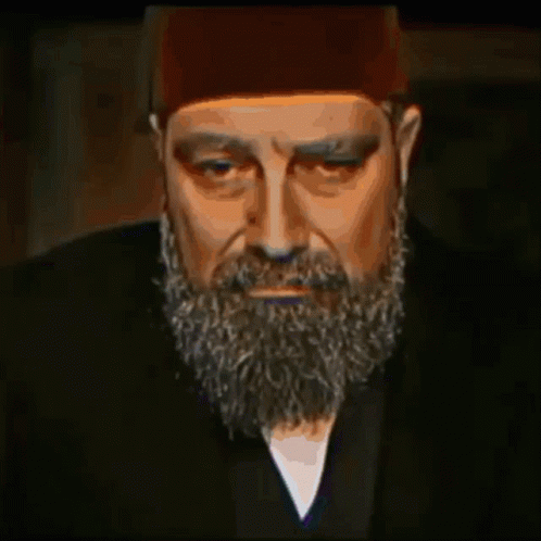 A Man With A Beard Wearing A Hat And A Black Jacket GIF