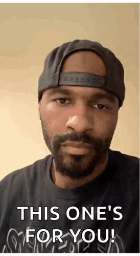 A Man With A Beard Wearing A Hat And A Black Shirt Says " This One 'S For You " GIF