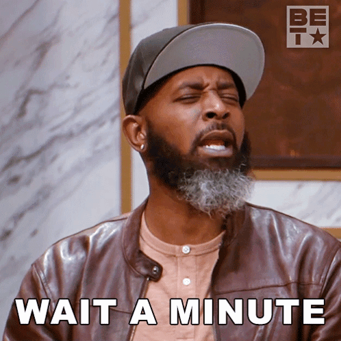 A Man With A Beard Wearing A Hat And A Leather Jacket Says " Wait A Minute " GIF
