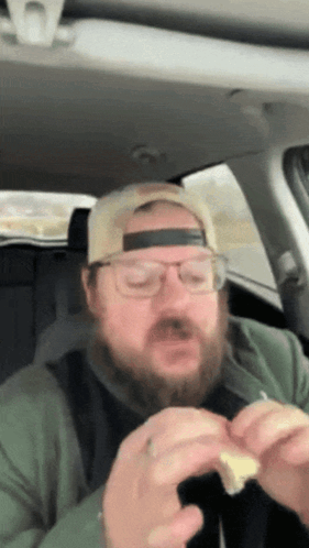 A Man With A Beard Wearing A Hat And Glasses Is Eating A Sandwich GIF