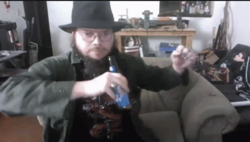 A Man With A Beard Wearing A Hat And Glasses Is Holding A Bottle Of Bud Light GIF