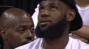 A Man With A Beard Wearing A Hat Is Sitting In A Stadium . GIF