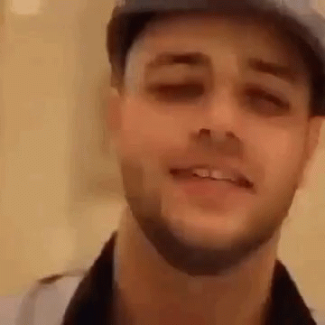 A Man With A Beard Wearing A Hat Is Smiling . GIF