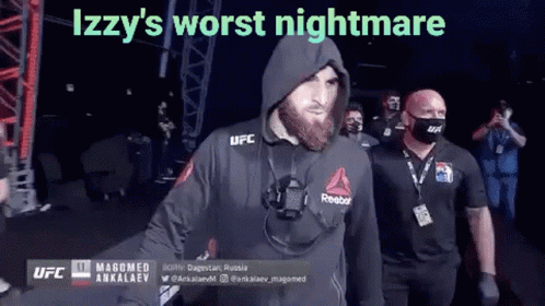 A Man With A Beard Wearing A Hooded Jacket And A Mask Is Walking Into A Ring . GIF