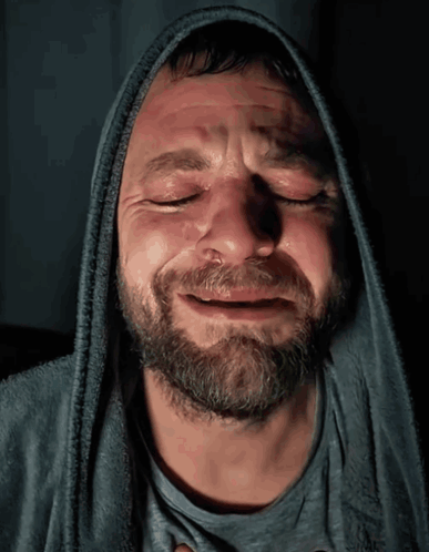a man with a beard wearing a hooded sweatshirt is crying with his eyes closed