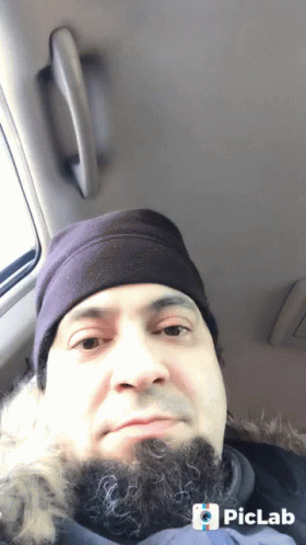 A Man With A Beard Wearing A Purple Hat Is Sitting In The Back Seat Of A Vehicle GIF