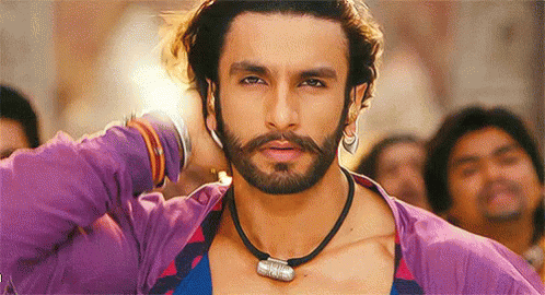 A Man With A Beard Wearing A Purple Shirt And A Black Necklace Is Standing In Front Of A Crowd . GIF