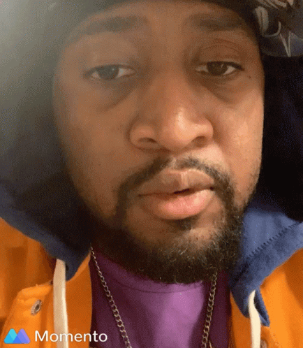 A Man With A Beard Wearing A Purple Shirt And A Momento Logo On The Bottom GIF