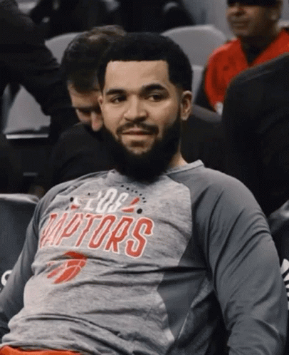 A Man With A Beard Wearing A Raptors Shirt Is Sitting In The Stands . GIF